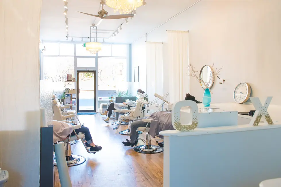 The Glow Facial Bar room: white treatment chairs in a row, a pale blue front counter and tall front windows
