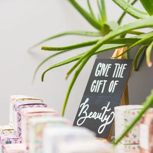 A chalkboard sign reading Give the gift of Beauty beside gift boxes and an aloe plant